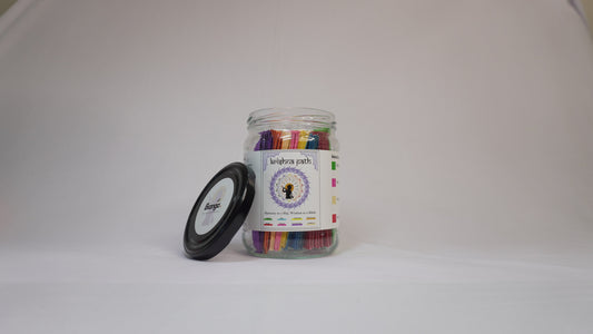 Krishna Path Gita Jar with colorful sachets in a glass jar on a plain white background, black lid placed beside the jar